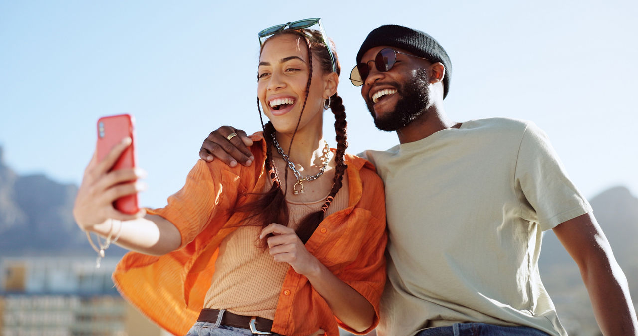 Fröhliches Paar macht ein Selfie im Sonnenschein, beide lachen und genießen den Moment.