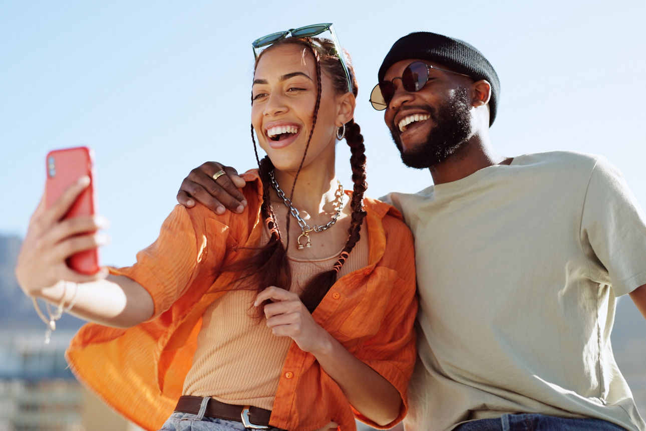 Fröhliches Paar macht ein Selfie im Sonnenschein, beide lachen und genießen den Moment.