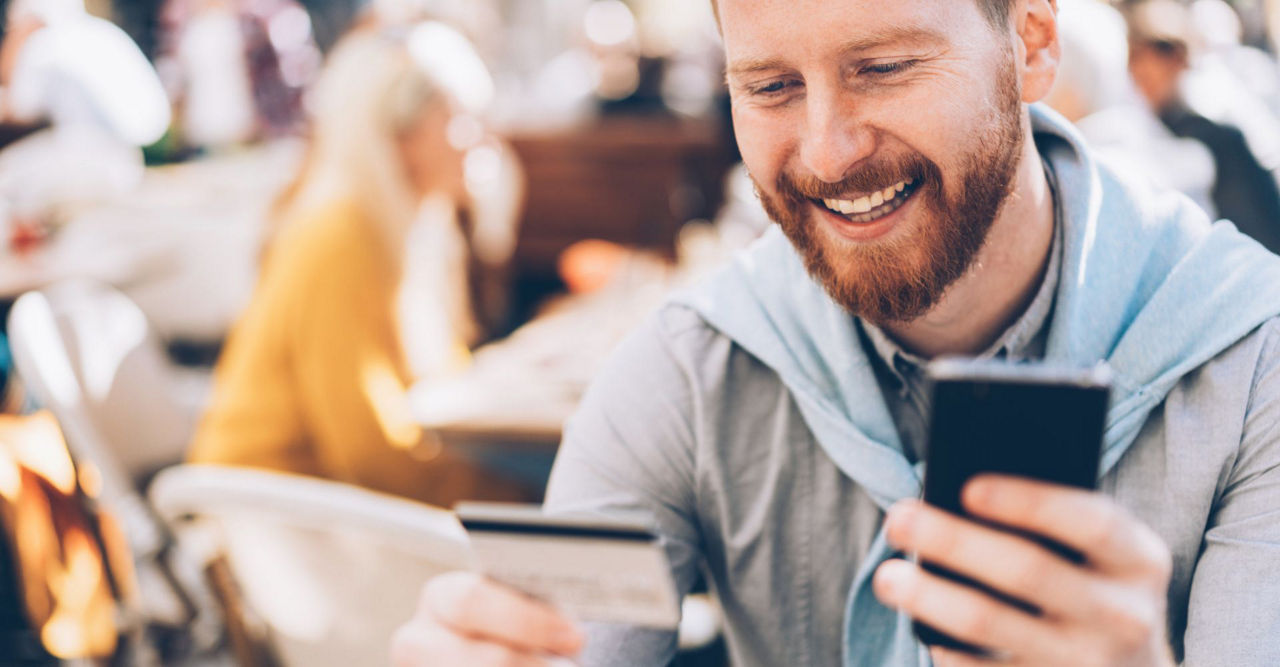 ein Mann schaut auf sein Handy und seine Bankcard