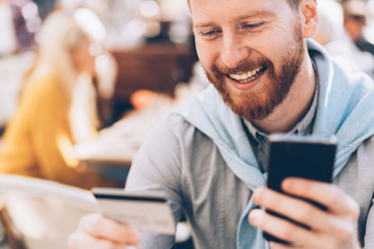 ein Mann schaut auf sein Handy und seine Bankcard