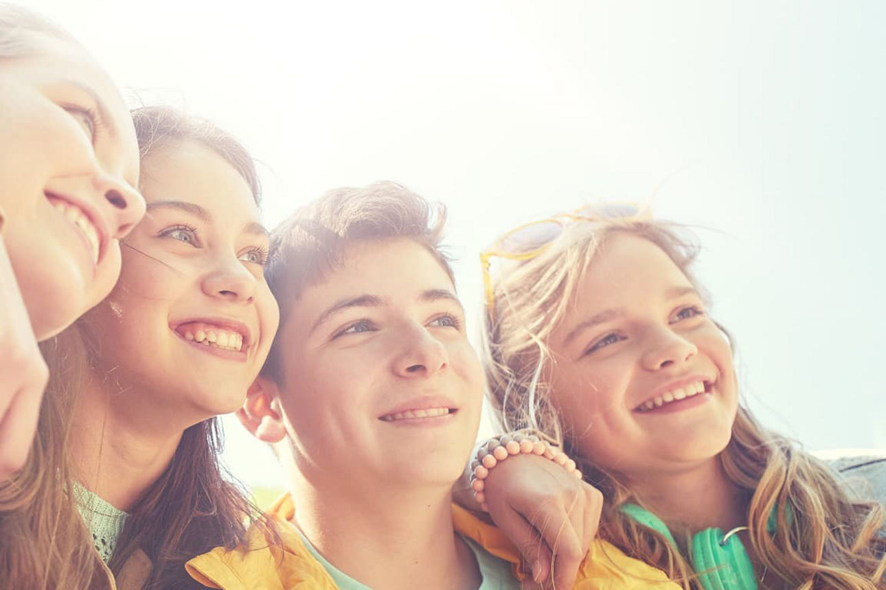 Vier Jugendliche umarmen sich jeweils an den Schultern und schauen lächelnd zur Seite