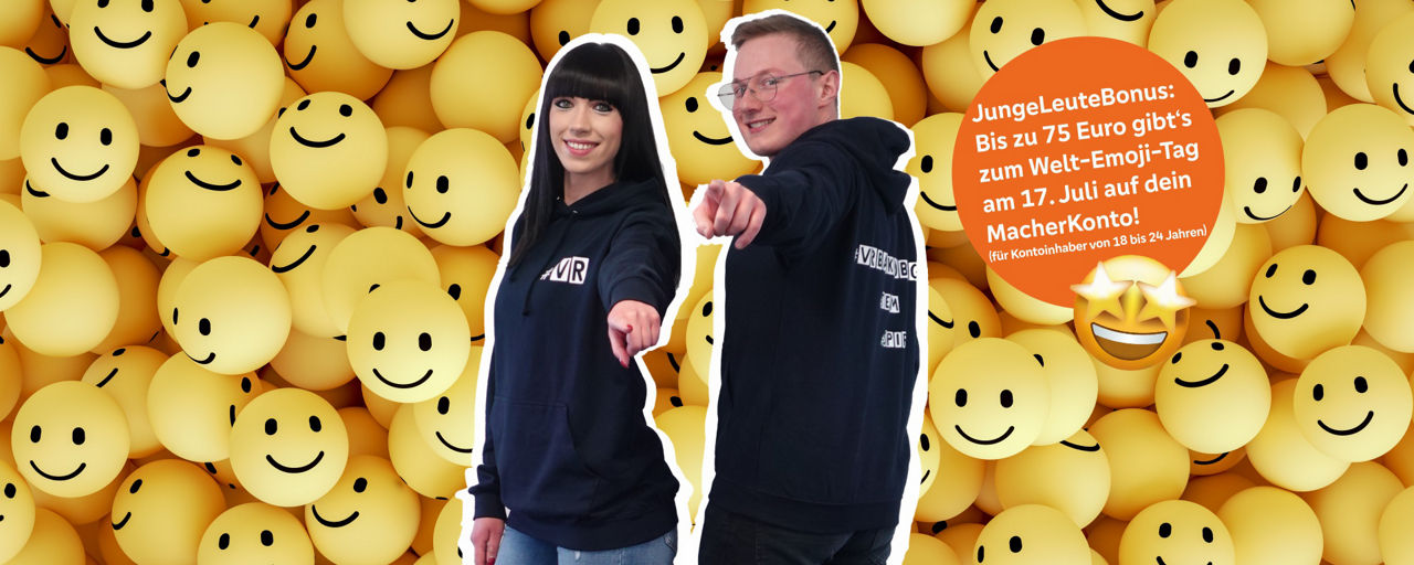 Zwei junge Menschen vor einer Wand mit Smileys deuten auf den Betrachter
