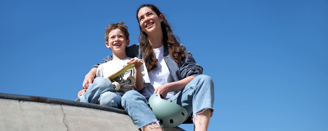Ein Junge mit Skateboard sitzt neben seiner Mutter