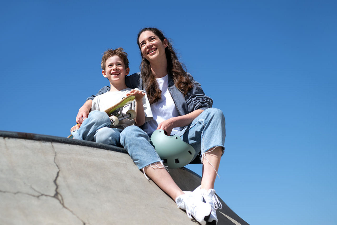 Ein Junge mit Skateboard sitzt neben seiner Mutter