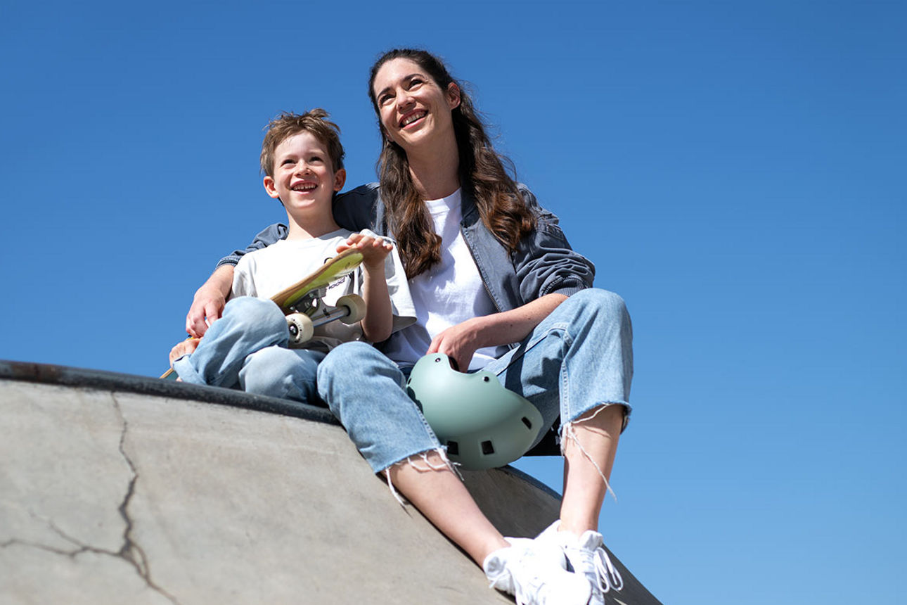 Ein Junge mit Skateboard sitzt neben seiner Mutter