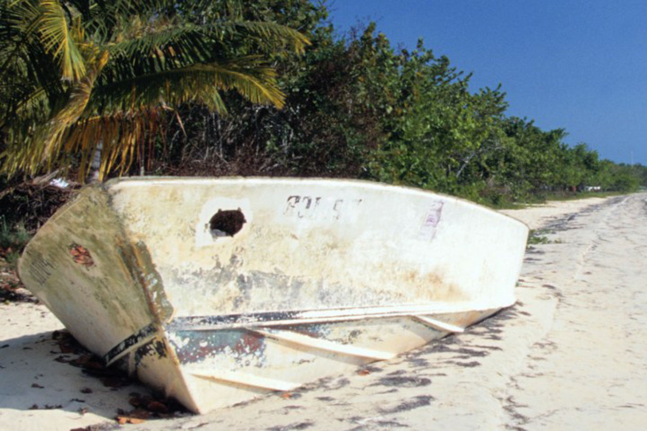Strand mit Boot, weißem Sand, Meer und blauem Himmel.
