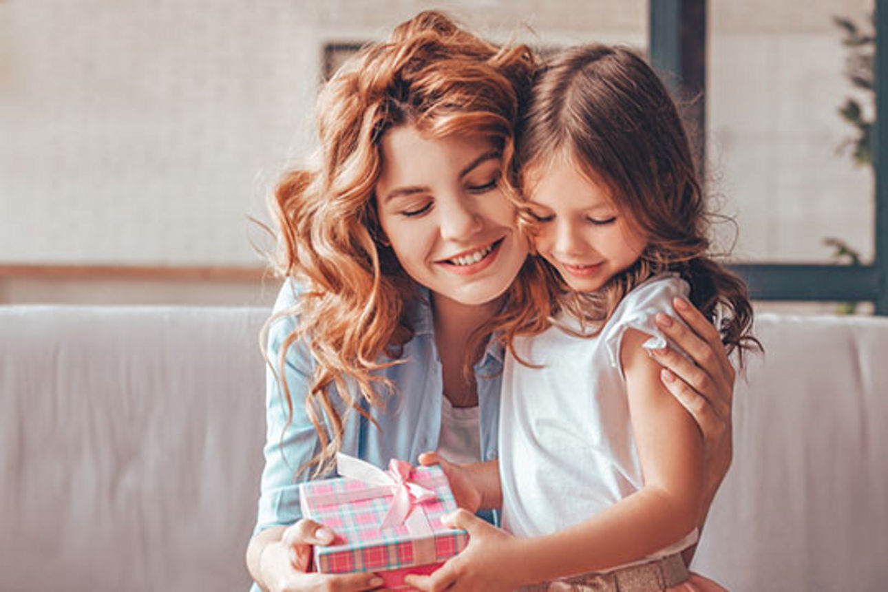 Eine Frau umarmt ein Mädchen, beide halten ein Geschenk