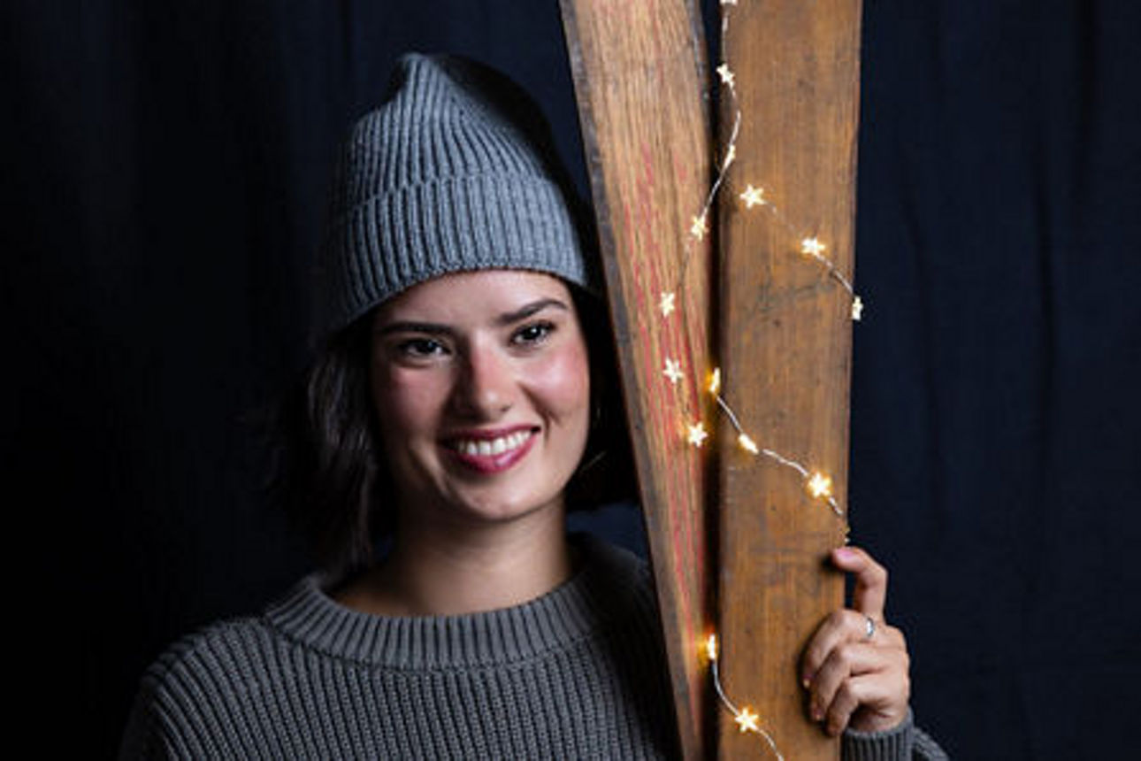 Eine Frau mit Mütze lehnt an einem Balken mit Lichterkette