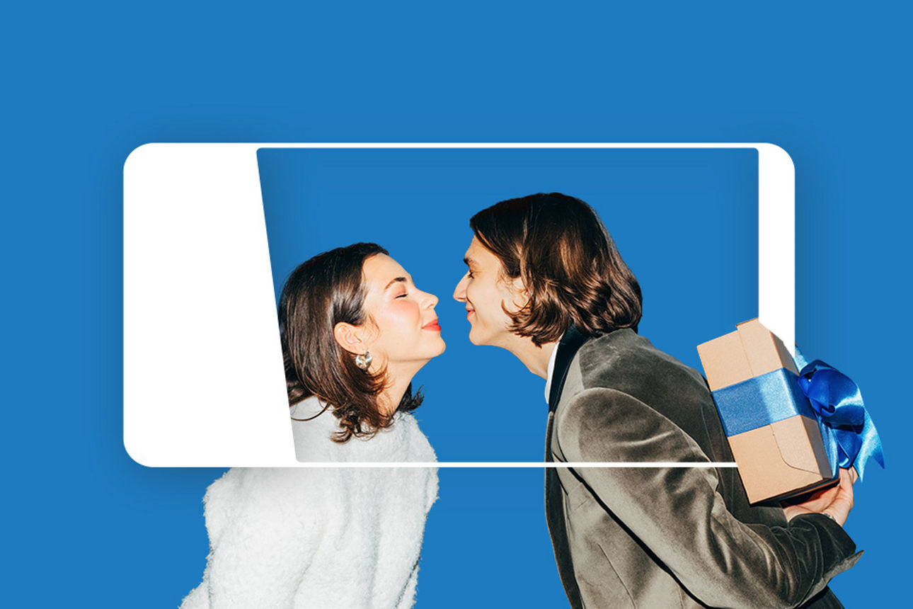 Eine Frau und ein Mann küssen sich zart. Der Mann versteckt ein Geschenk hinter seinem Rücken.