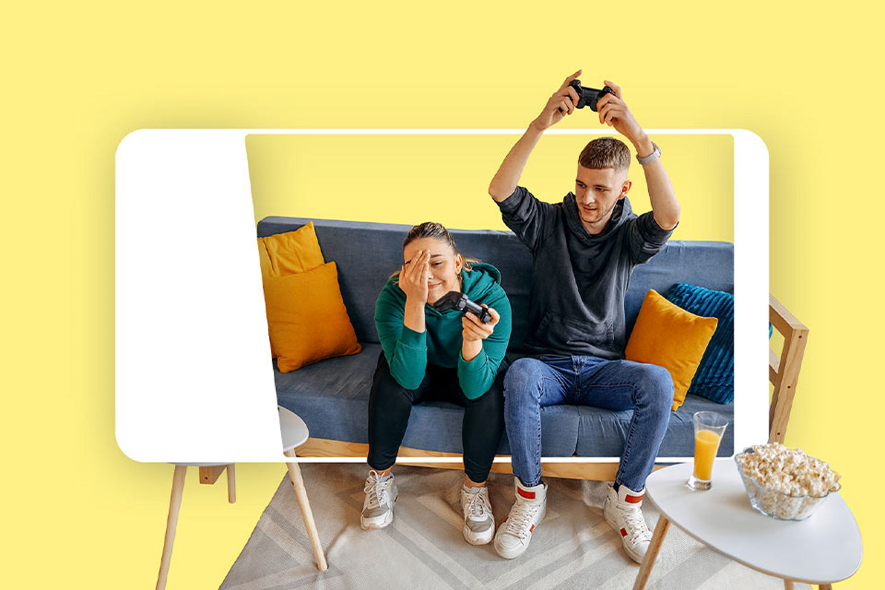 Zwei Personen auf einer Couch, die mit einer Spielconsole spielen.