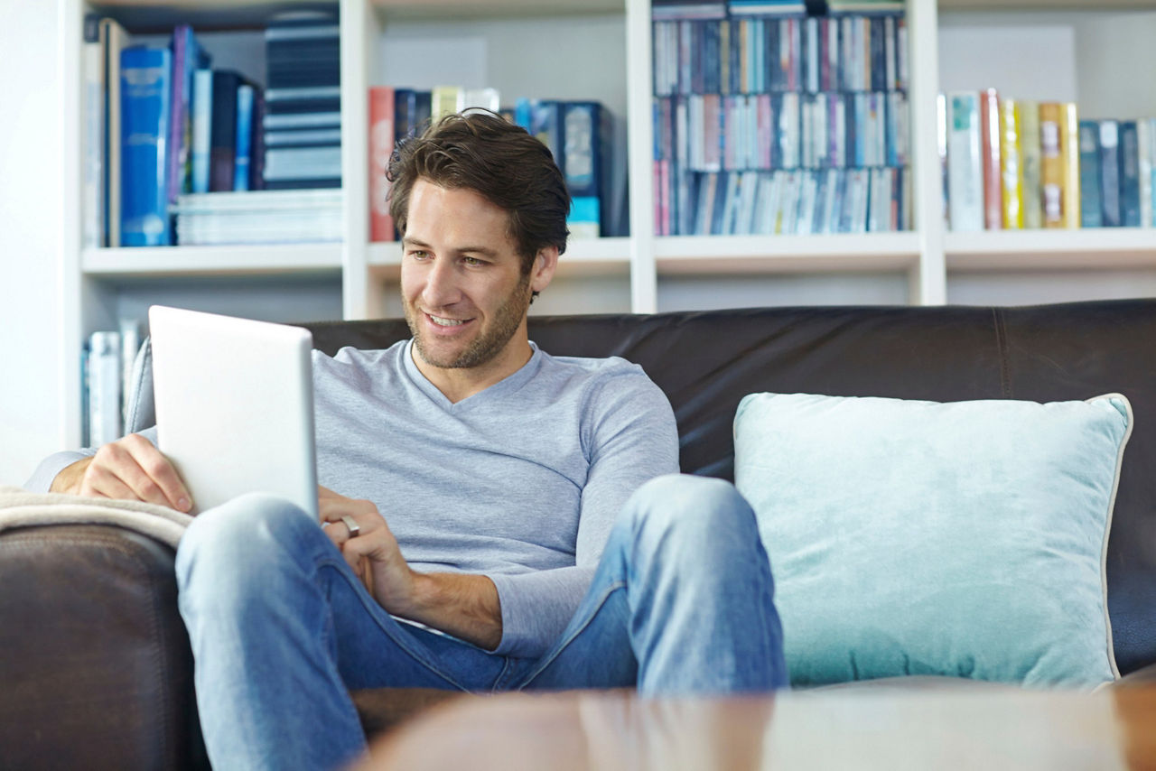 Mann mit Tablet in der Hand sitzt auf Sofa