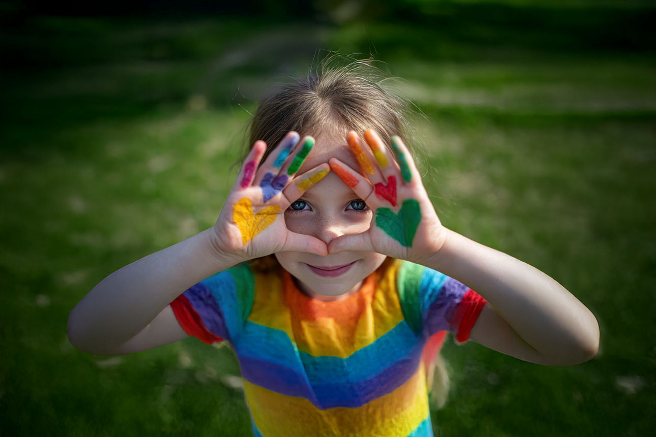 Kind mit buntem T-Shirt hält Hände mit gelber, roter und grüner Farbe vor sich