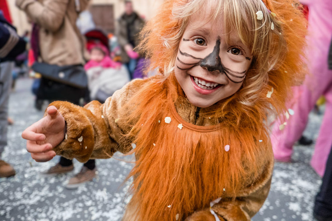 Ein Kind im Löwenkostüm am Straßenrand beim Karnevalsumzug.
