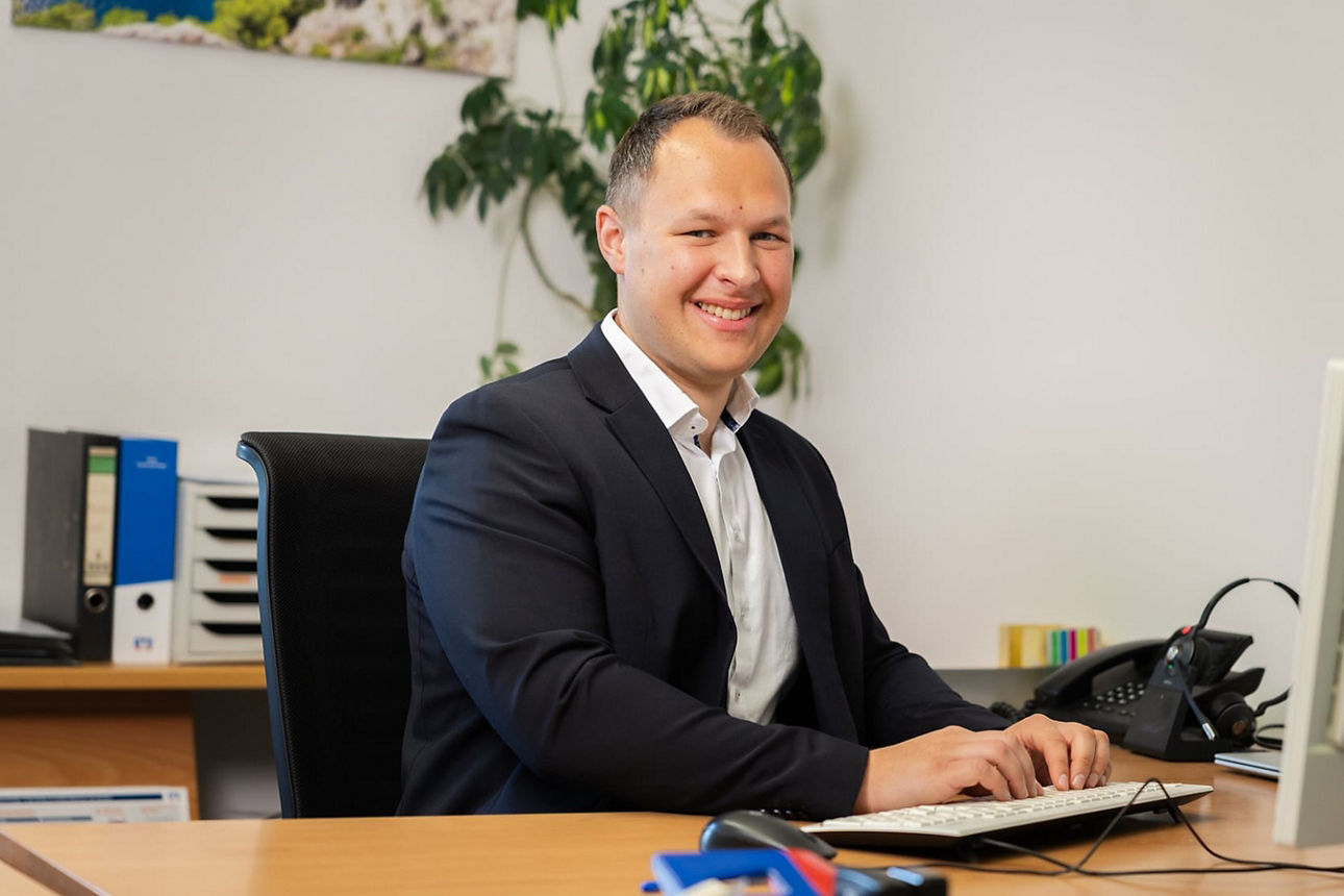 Lachender Mann im Anzug sitzt am Schreibtisch und arbeitet. Professionelle und freundliche Büroatmosphäre. 