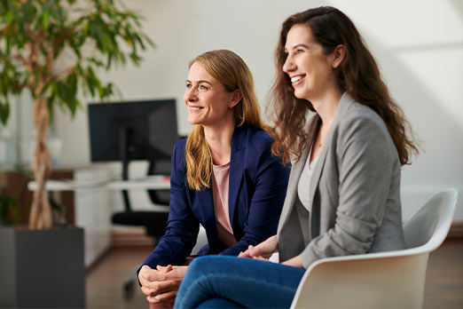 Zwei lächelnde Frauen sitzen nebeneinander in einem Büro