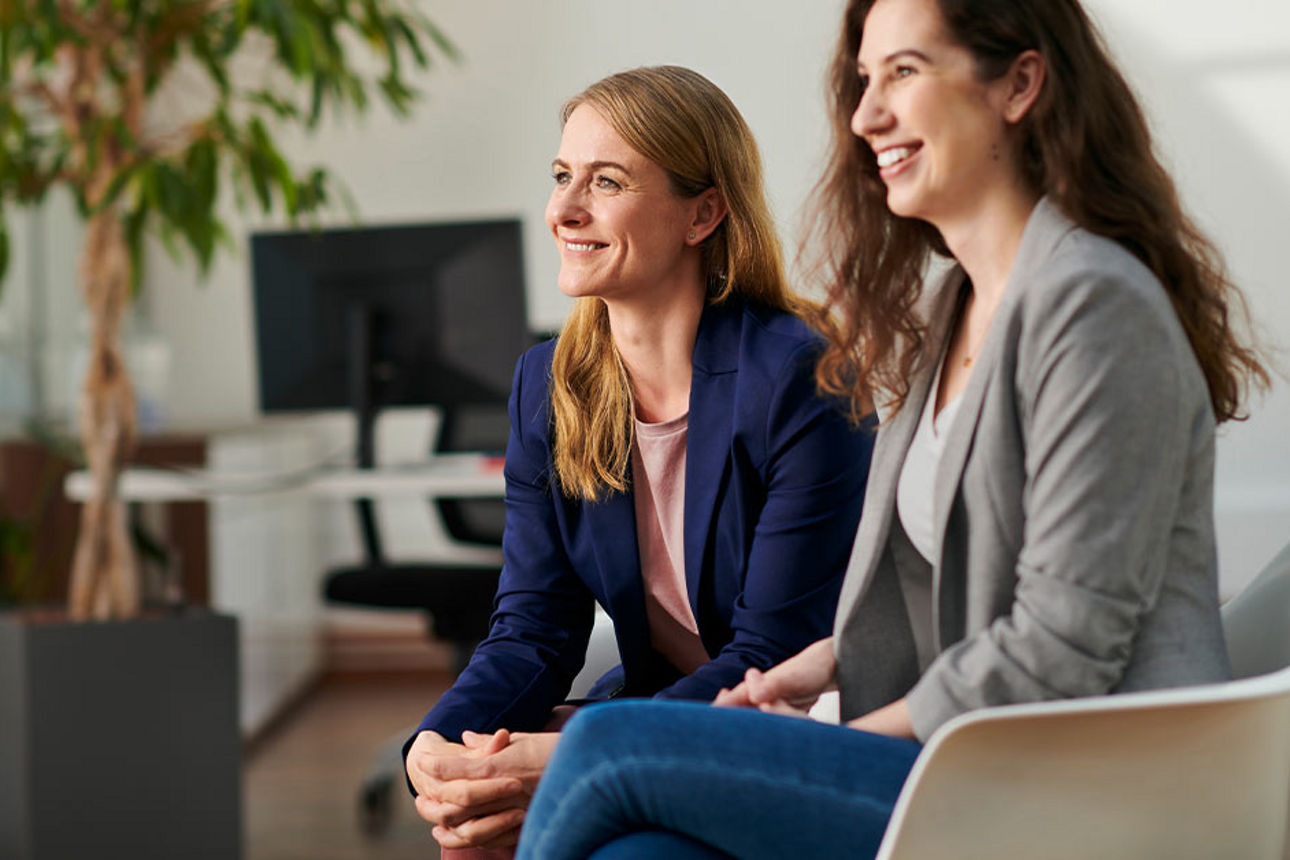 Zwei Frauen sitzen nebeneinander und lächeln 