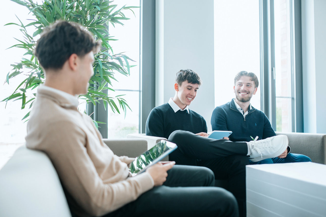 Drei junge Männer sitzen lächelnd in einem Besprechungsraum