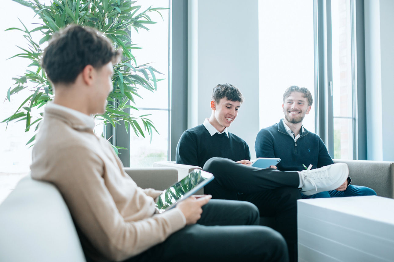 Drei junge Männer sitzen lächelnd in einem Besprechungsraum