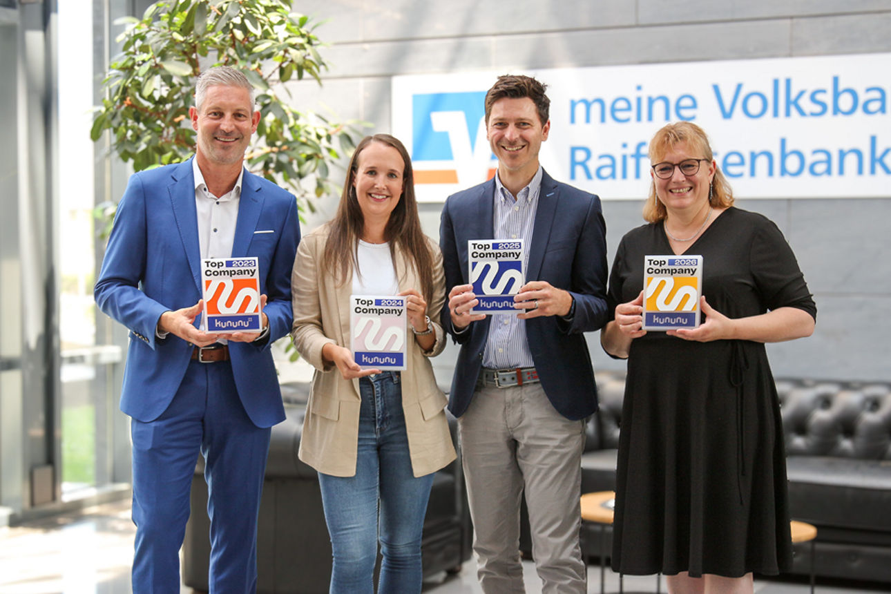 Vier Mitarbeitende präsentieren Kununu-Arbeitgebersiegel vor dem Eingangsbereich der meine Volksbank Raiffeisenbank.