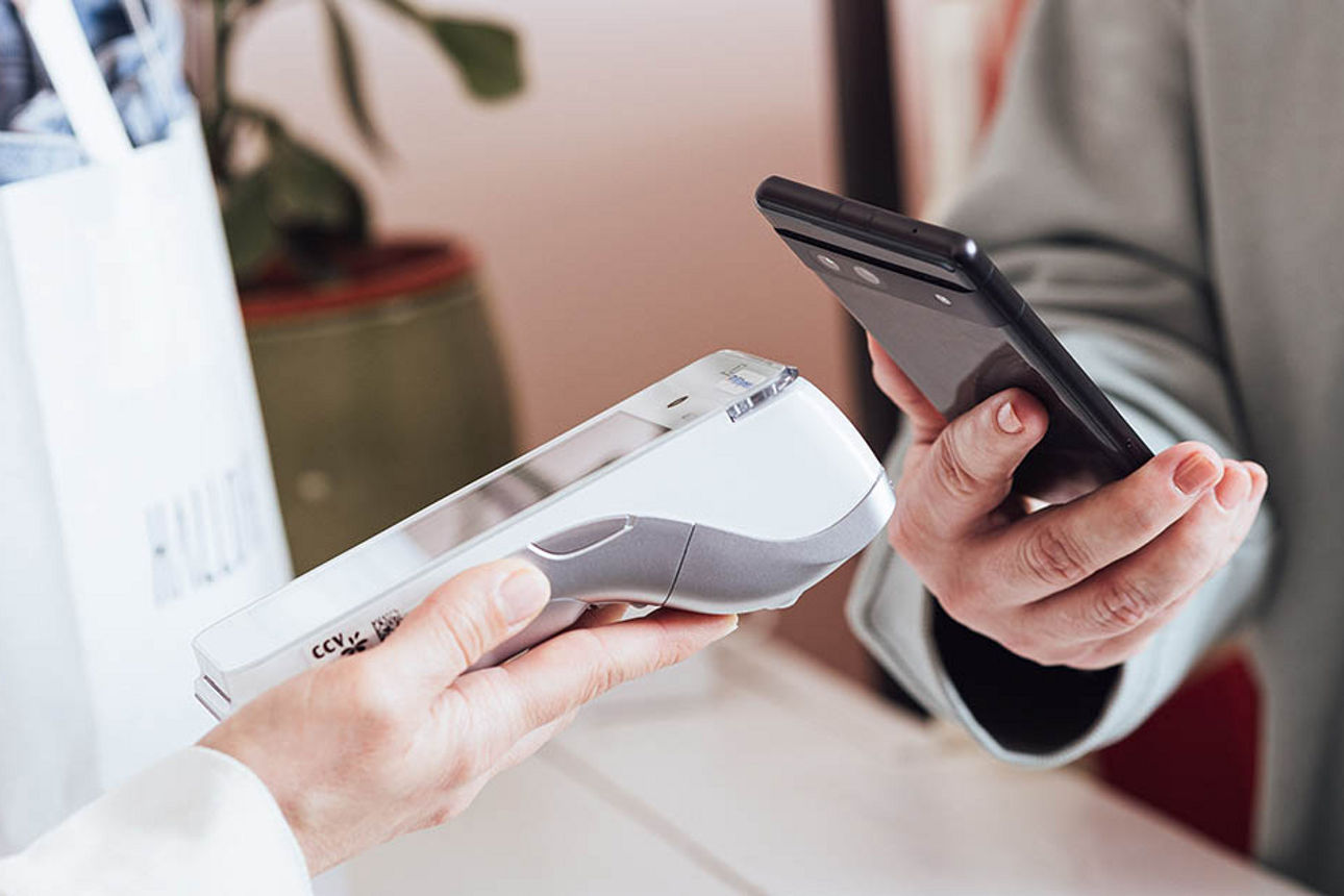 Person hält Karte über mobiles Kartenterminal zur kontaktlosen Zahlung