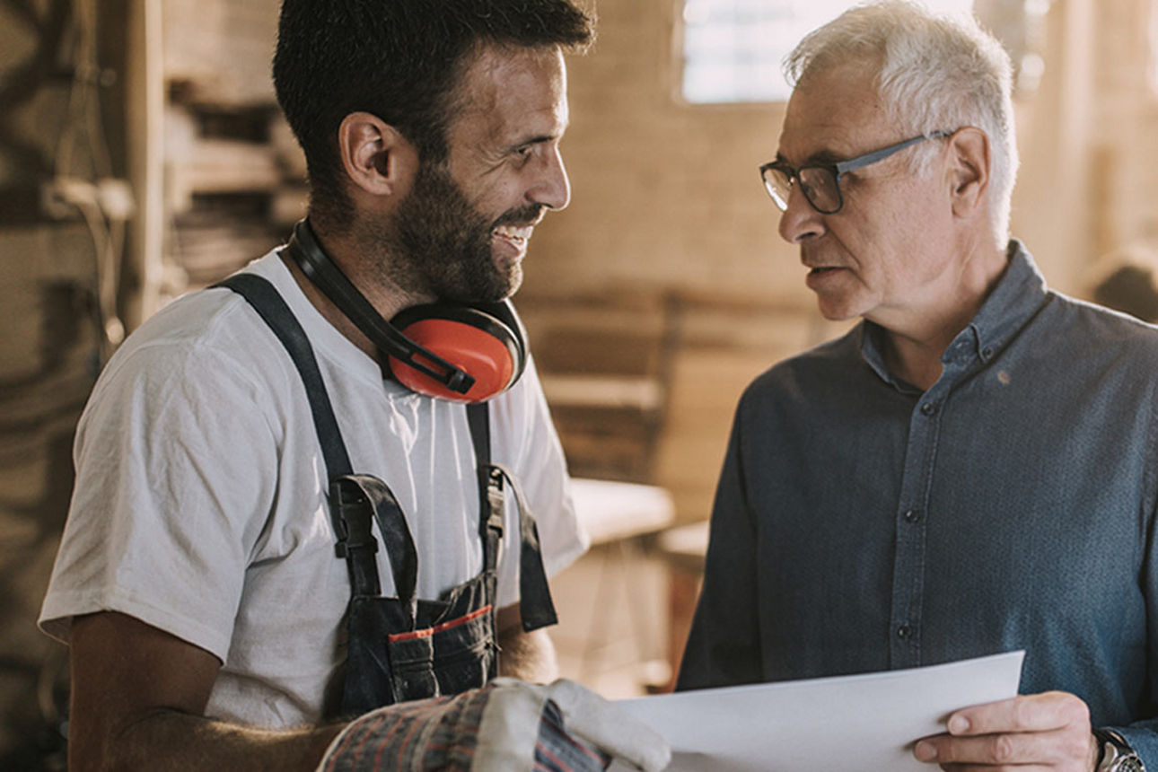 Zwei Männer in einer Werkstatt, die ein Dokument besprechen