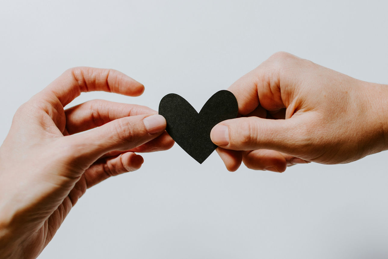 Zwei Hände, die sich ein schwarzes Herz aus Papier reichen