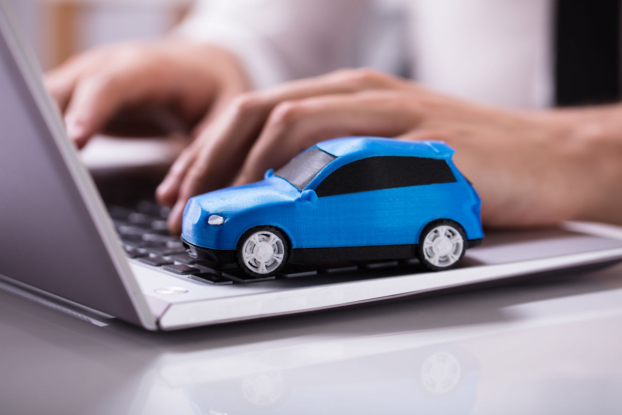 Blaues Spielzeugauto steht auf einem Laptop während die Person vor dem Laptop eine Kfz Versicherung abschließt