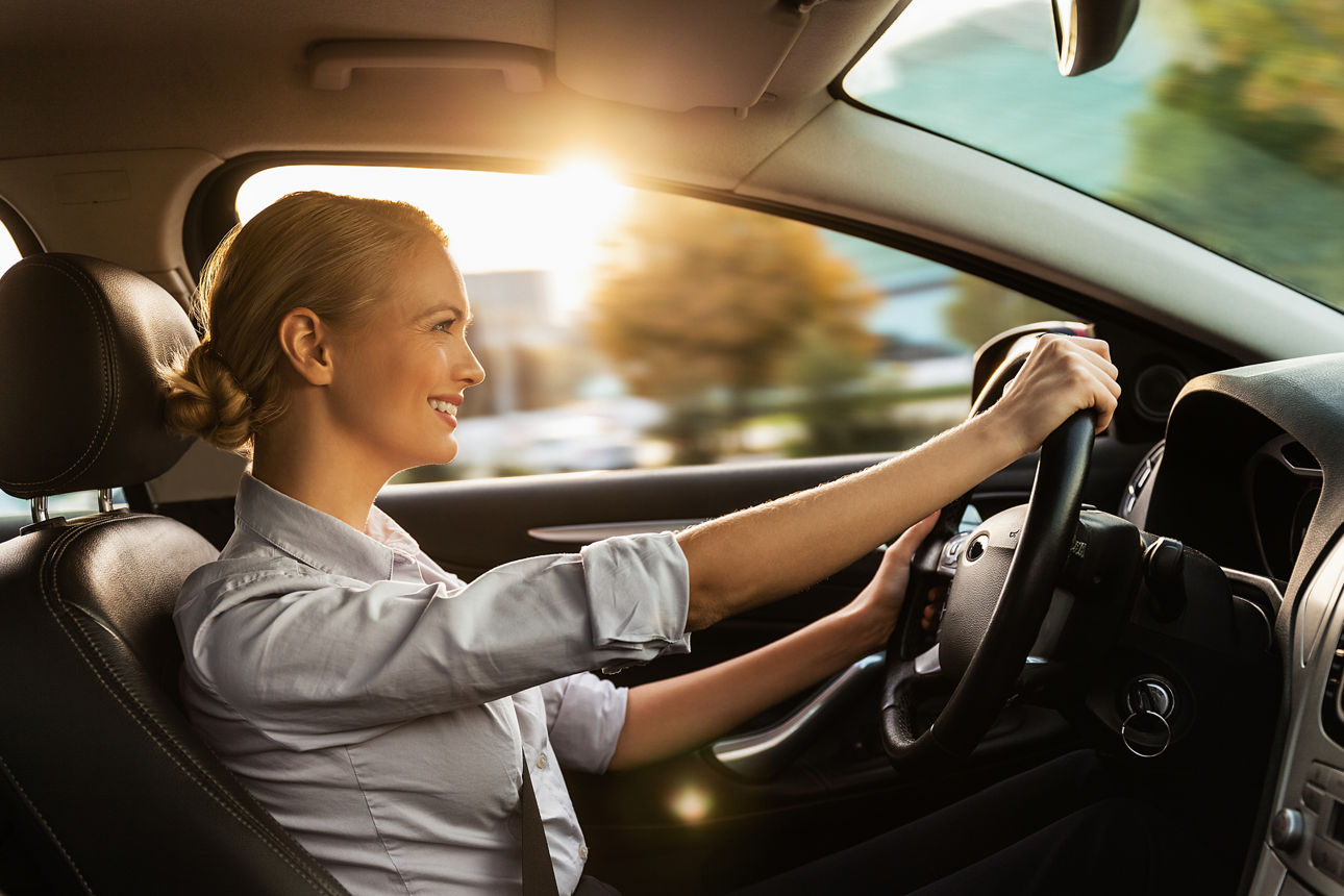 Geschäftsfrau sitzt in ihrem Auto am Steuer und ist glücklich weil sie eine Kfz Versicherung abgeschlossen hat