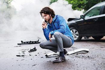 Mann telefoniert in der Hocke nach einen Schaden am Auto