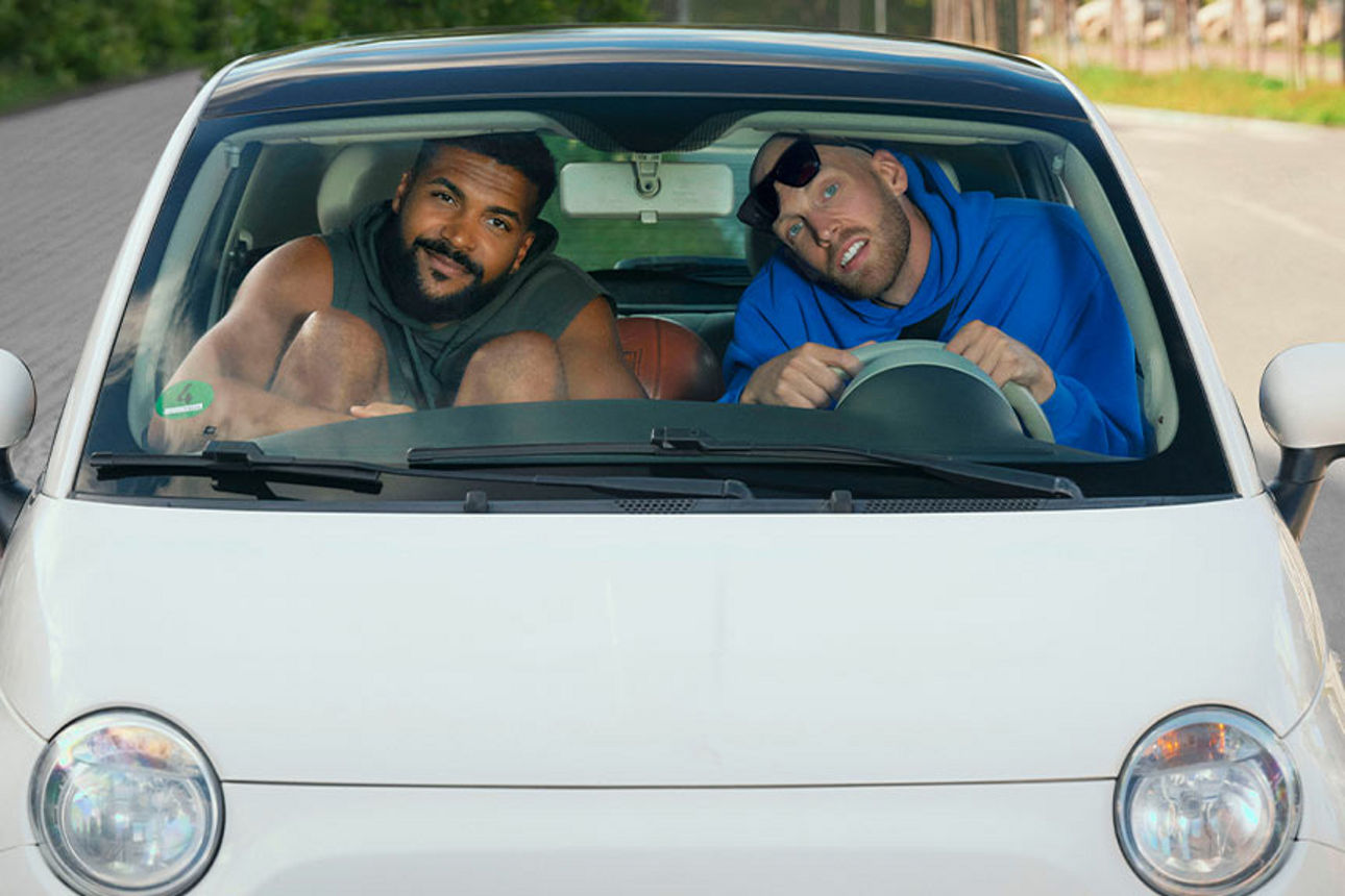 Ein Mann hockt vor einem beschädigten Auto und telefoniert