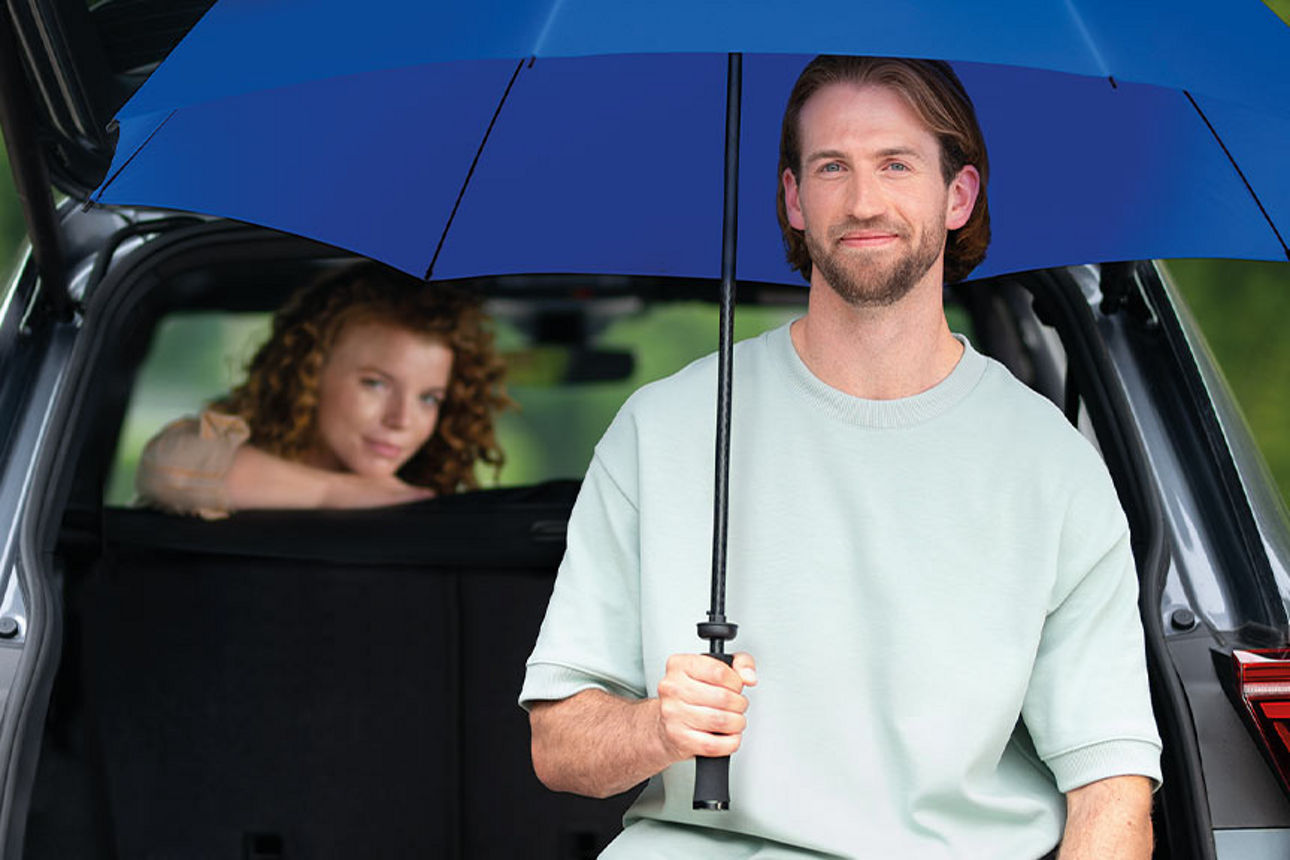 Mann und Frau unter einem Schirm neben ihrem Auto und Motorrad