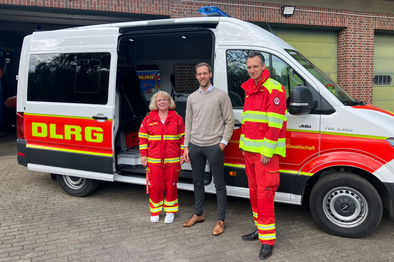 Zwei Männder und eine Frau stehen vor einem DLRG Bus