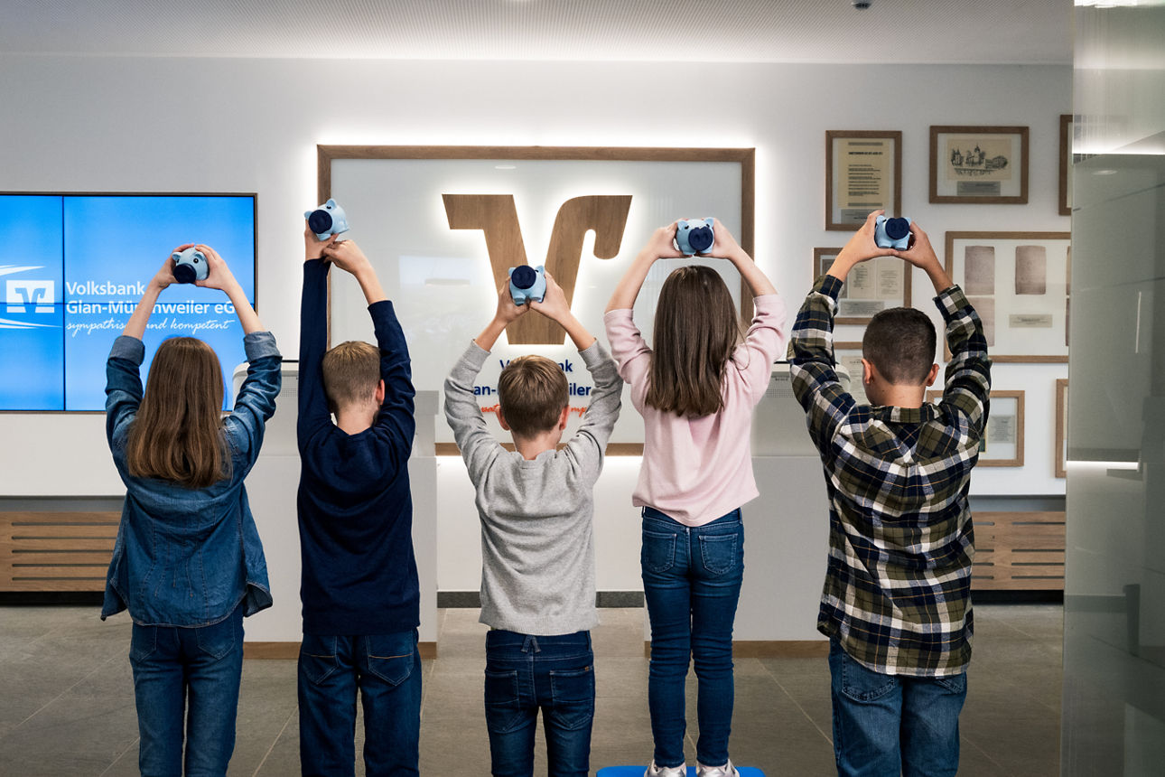 5 Kinder die gemeinsam mehrere Sparschweine hochhalten