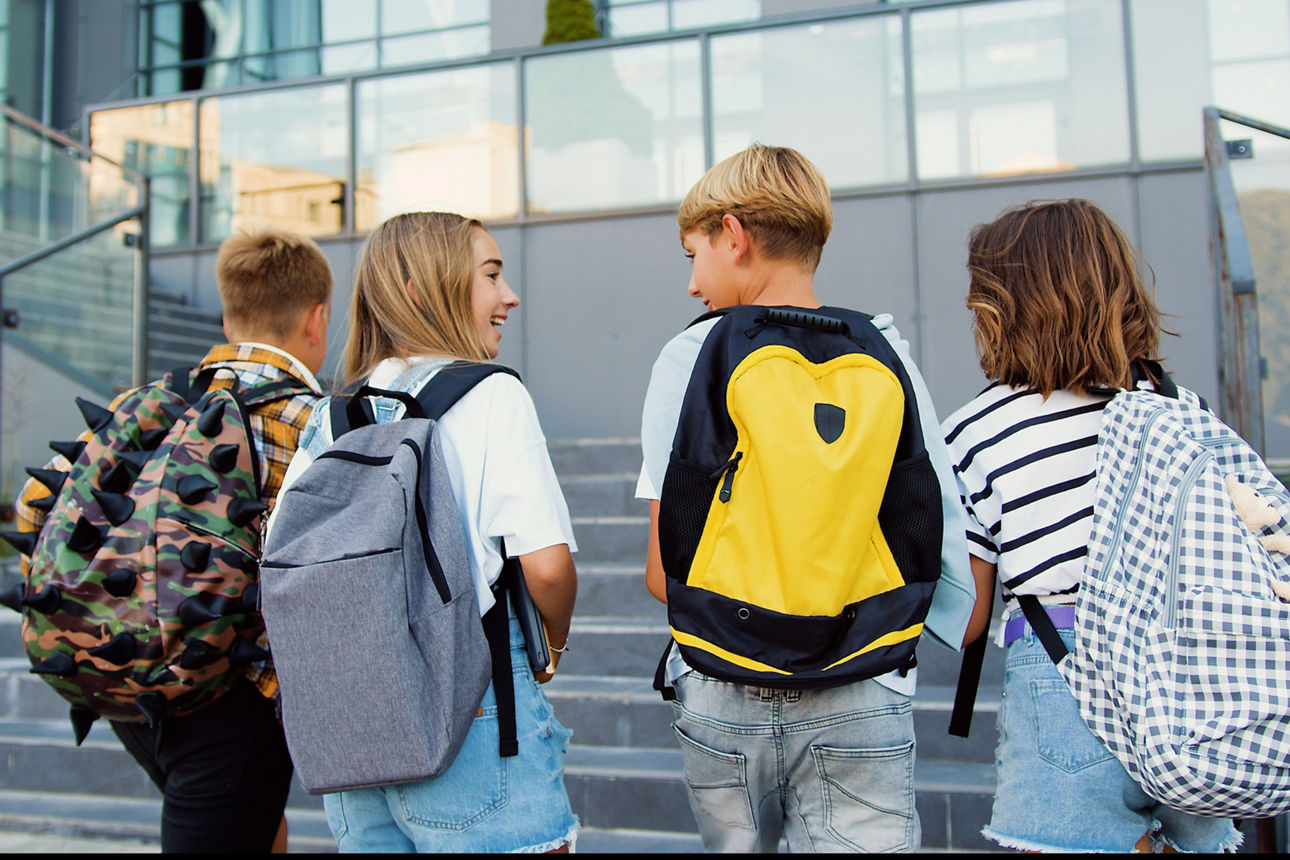 4 Kinder mit Schulranzen laufen in Richtung Schule