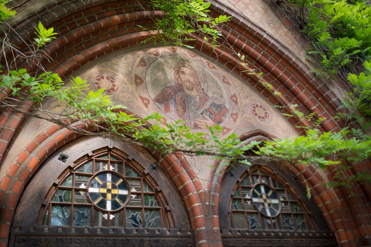 Detailansicht eines alten, rot verblendeten Backsteinportals einer Kirche mit zwei runden bleiverglasten Fenstern. 