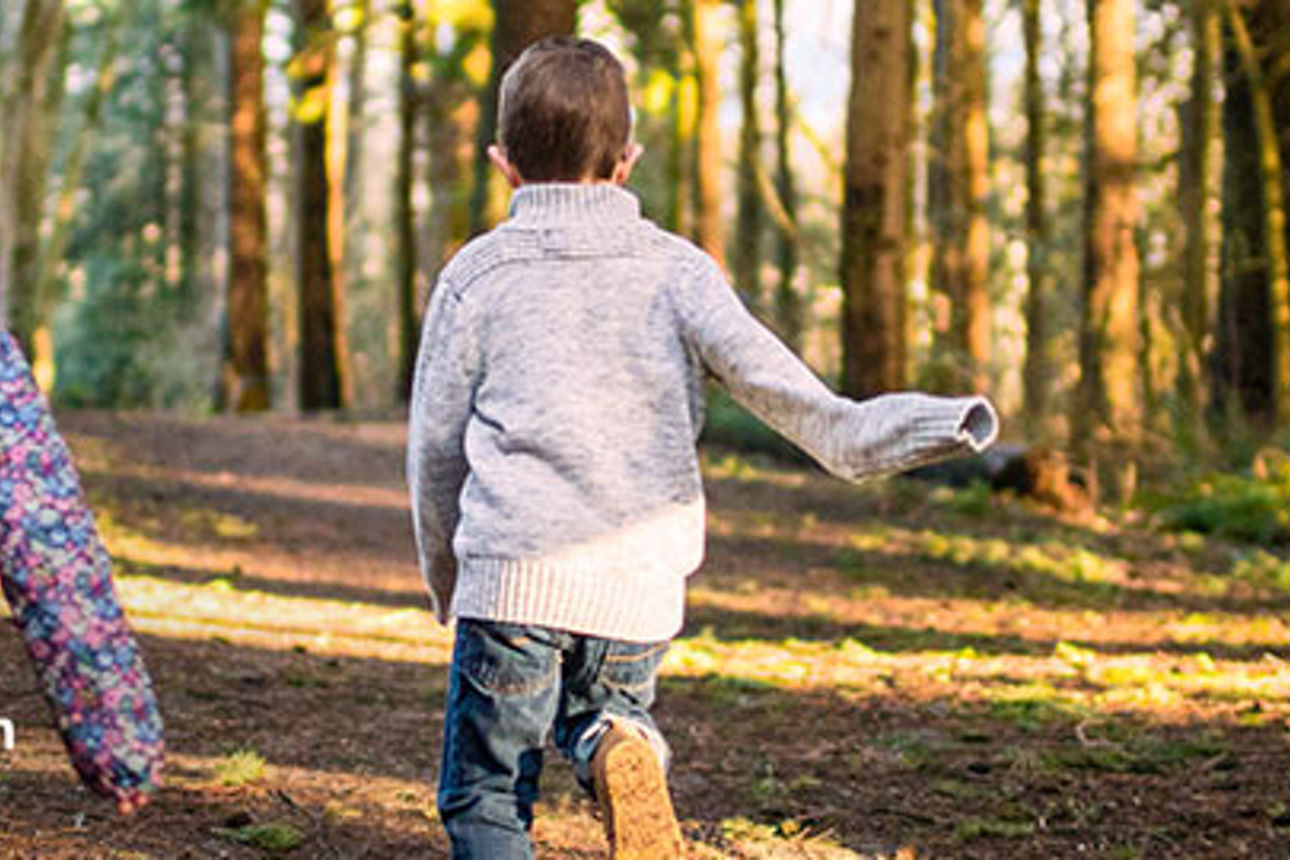 Zwei Kinder rennen vergnügt durch einen üppigen grünen Wald, umgeben von hohen Bäumen und gedämpftem Sonnenlicht. 
