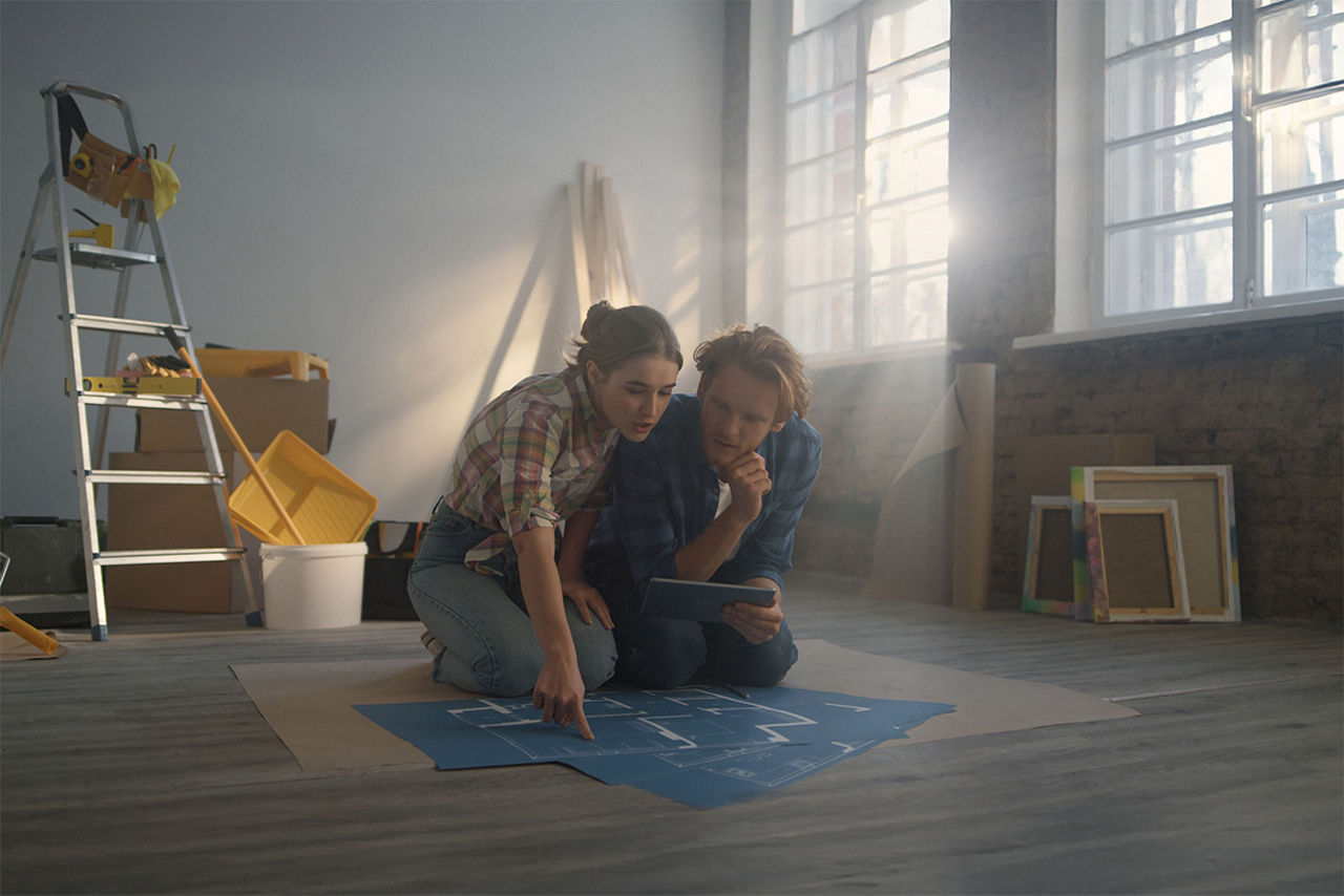 Pärchen sitzt mit einem Bauplan in einer Wohnung