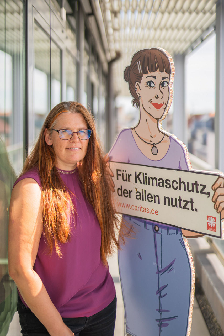 Vera Bünnagel neben einer Pappfigur mit dem Claim "Klimaschutz, der allen nutzt"