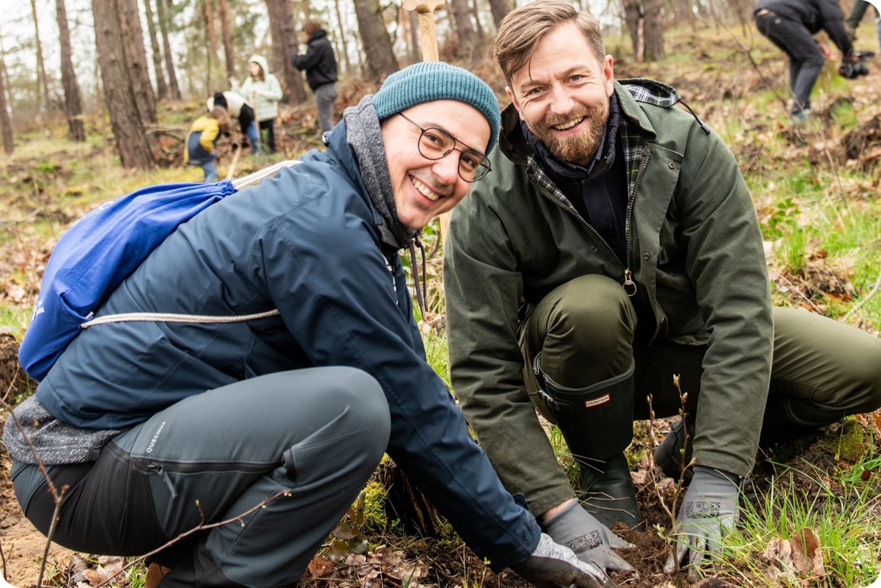Zwei Männer hocken im Wald und pflanzen einen Baumsetzling
