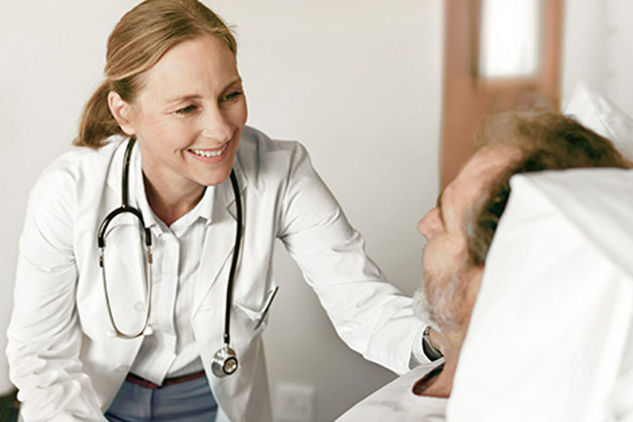 Eine Ärztin beugt sich freundlich lächelnd zu Ihrem Patienten