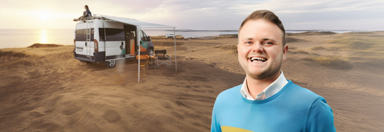 Mann steht lächelt in den Dünen vor einem Camper im Sonnenuntergang
