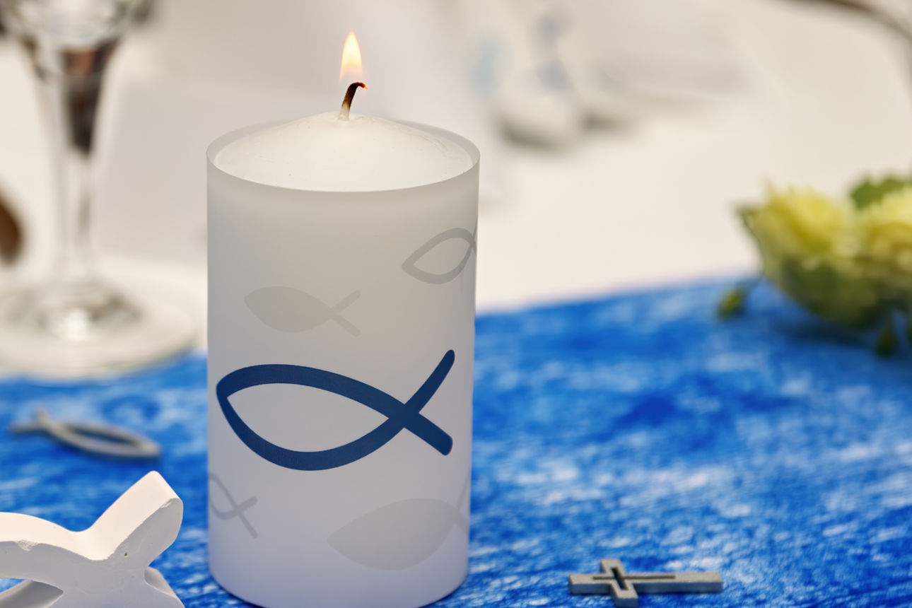 Eine brennende Kerze mit Fischsymbol auf einem festlichen gedeckten Tisch