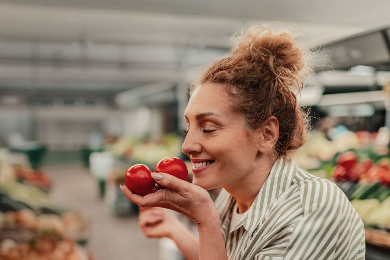 Eine lächelnde Frau hält in einem Supermarkt zwei Tomaten in der Hand.
