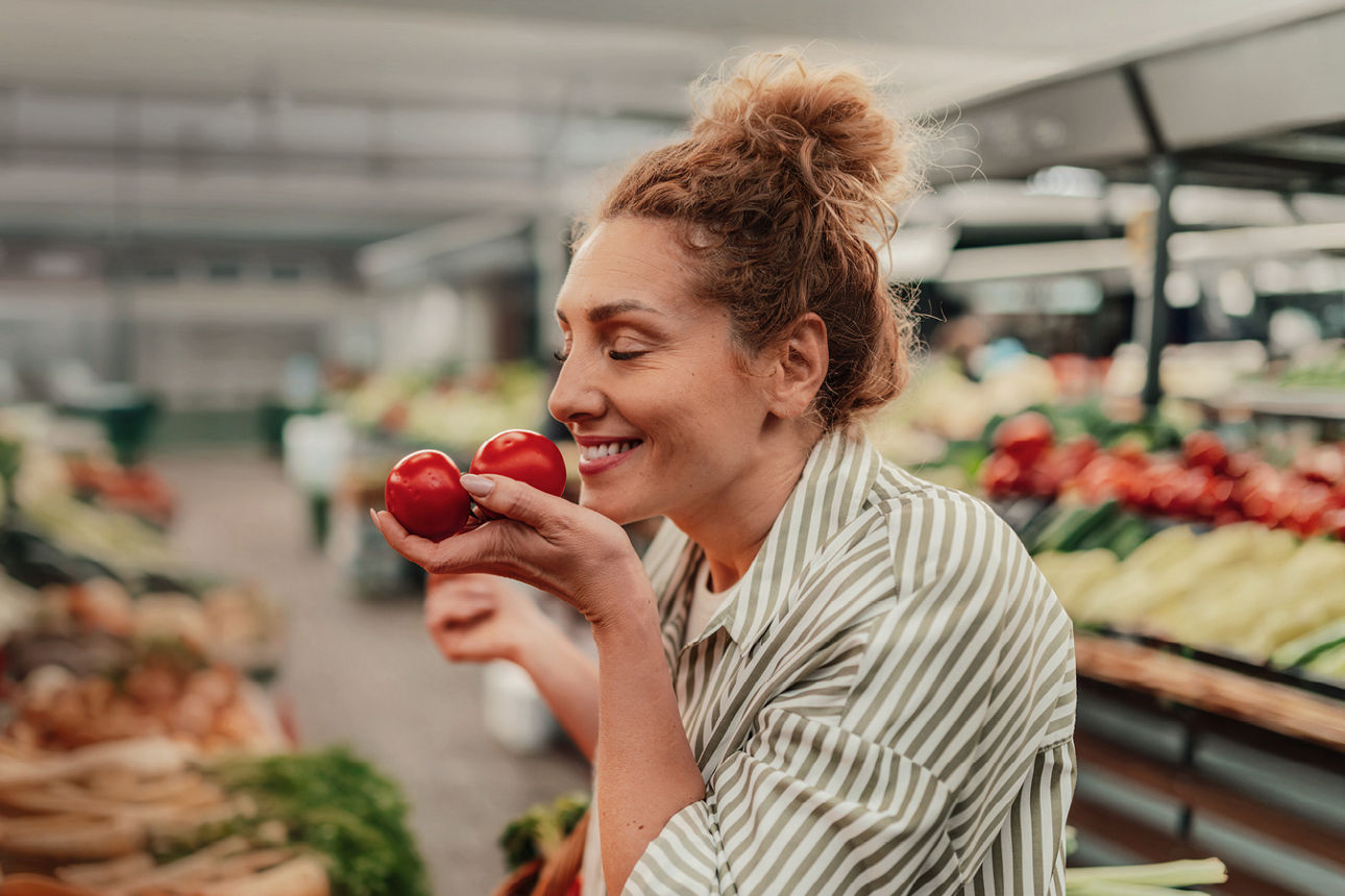 Eine lächelnde Frau hält in einem Supermarkt zwei Tomaten in der Hand.