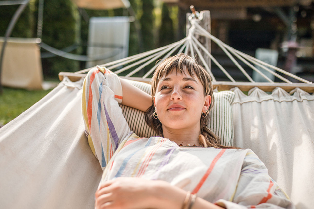 Person liegt in einer Hängematte im Garten bei Tageslicht.