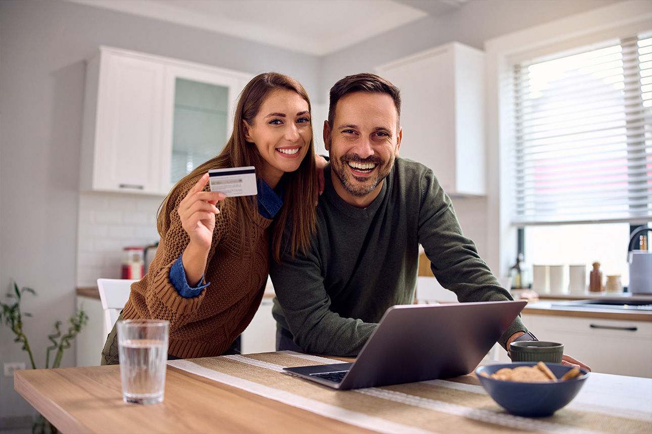 Pärchen sitzt glücklich vor einem Laptop und halten eine girocard in der hand
