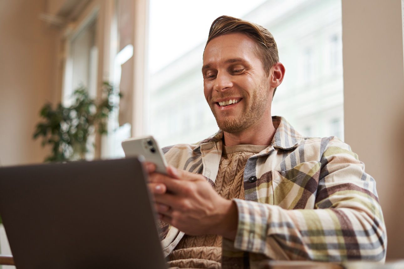Portrait eines glücklichen Mannes mit Handy sitzend vor Laptop
