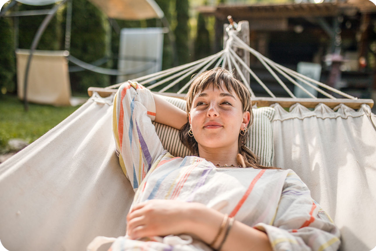 Person liegt in einer Hängematte im Garten bei Tageslicht.
