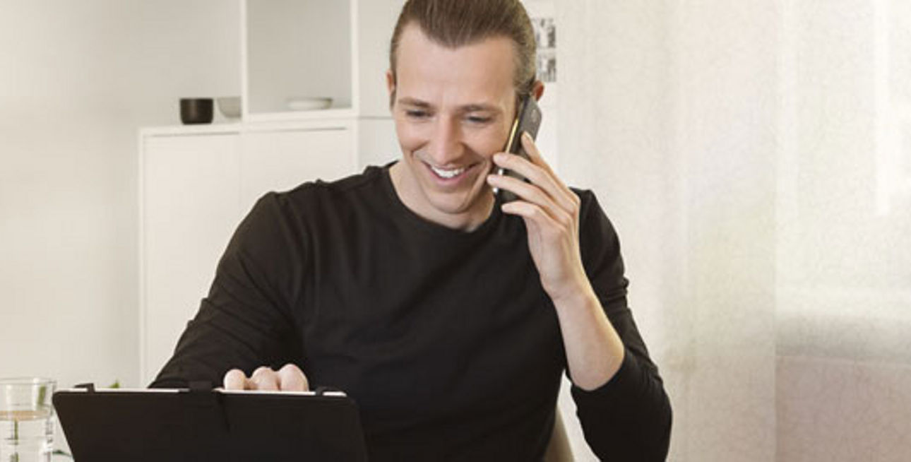 Ein Mann sitzt am Laptop und telefoniert mit einem Handy