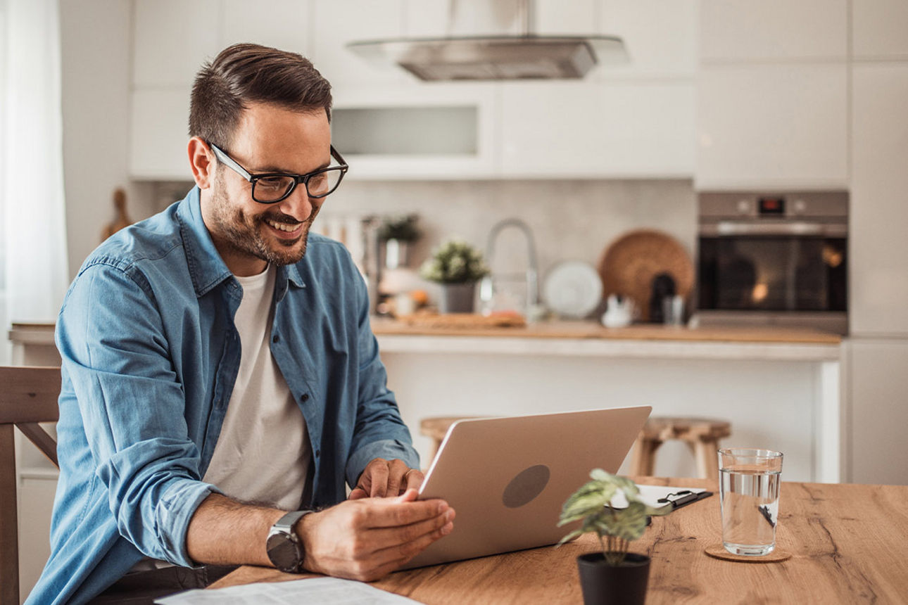 Mann im blauen Hemd sitzt am Tisch mit Laptop